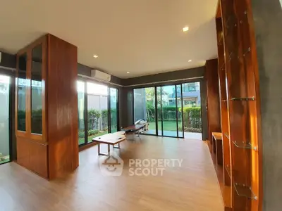 Spacious modern living room with large windows and wooden accents overlooking a lush garden.