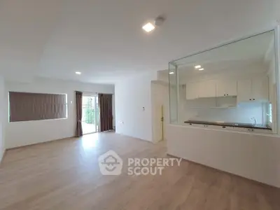 Spacious open-plan living room with large windows and modern kitchen view.