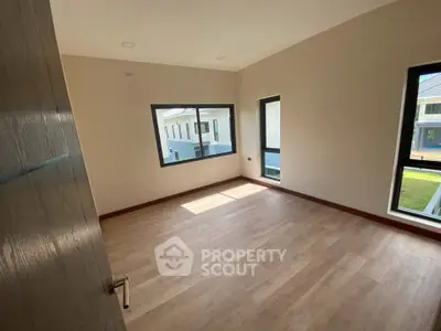 Spacious empty bedroom with large windows and wooden flooring in modern home.