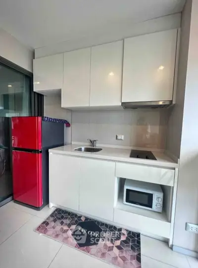 Modern compact kitchen with sleek cabinetry and red fridge in a stylish apartment.