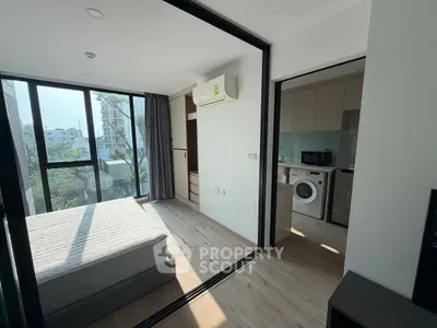 Modern bedroom with large windows and adjacent kitchen featuring washing machine and microwave.