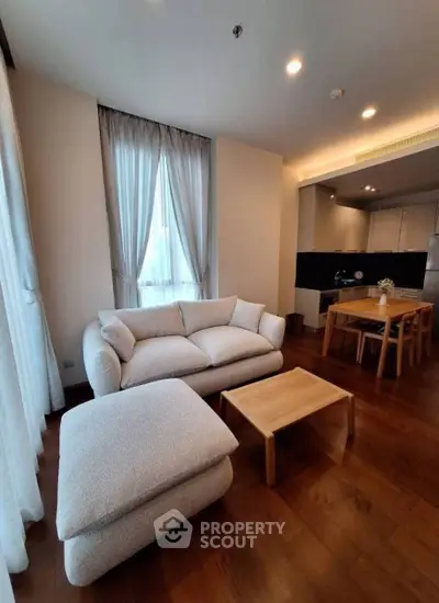 Modern living room with cozy sofa and open kitchen layout, featuring elegant wooden flooring and natural light.
