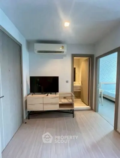 Modern living room with TV and air conditioning, leading to bathroom and bedroom.