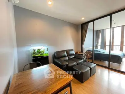 Modern living room with leather sofa, wooden table, and glass partition leading to bedroom.