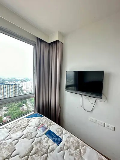 Cozy bedroom with wall-mounted TV and stunning city view from large window.