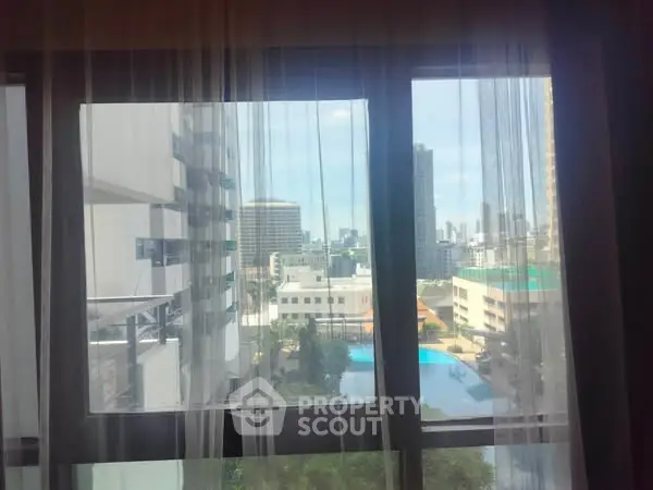 Cityscape view from window with sheer curtains and pool in sight.
