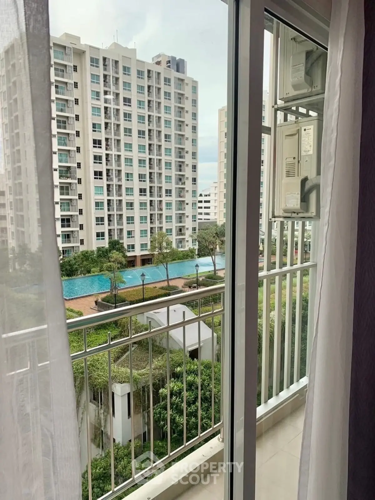 Stunning balcony view of modern high-rise with pool and lush greenery.