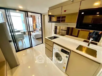 Modern kitchen with washing machine and open layout leading to living area.