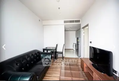 Modern living room with sleek black leather sofa and flat-screen TV, open to dining area and kitchen.