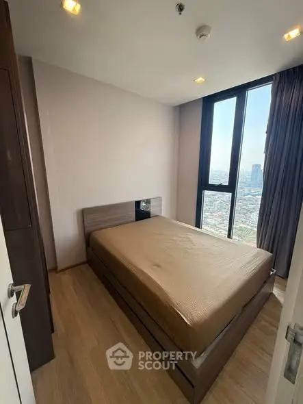 Modern bedroom with city view, featuring large windows and sleek wooden flooring.