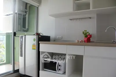 Modern kitchen with sleek cabinetry, compact fridge, and microwave in a bright apartment.