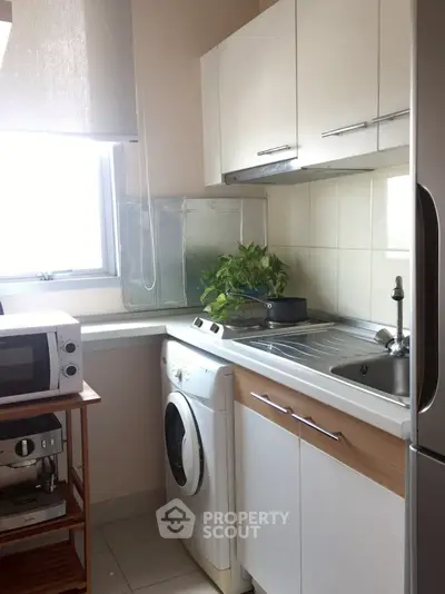 Compact kitchen with washing machine and microwave, featuring modern cabinetry and a bright window.