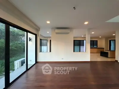 Spacious modern living room with hardwood floors and large windows overlooking garden