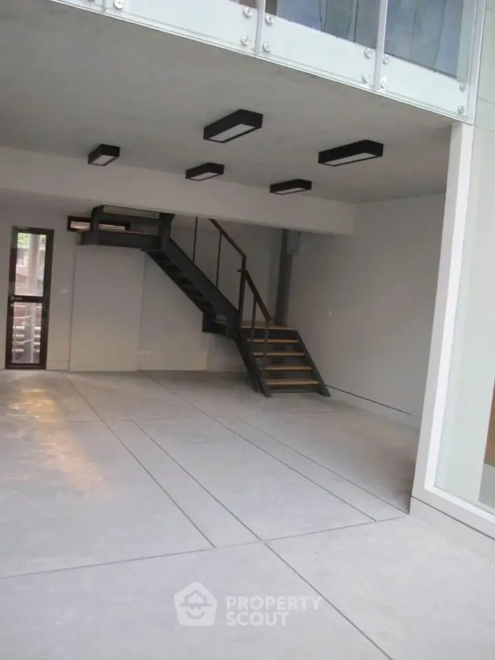 Modern open-plan living space with sleek staircase and large windows.