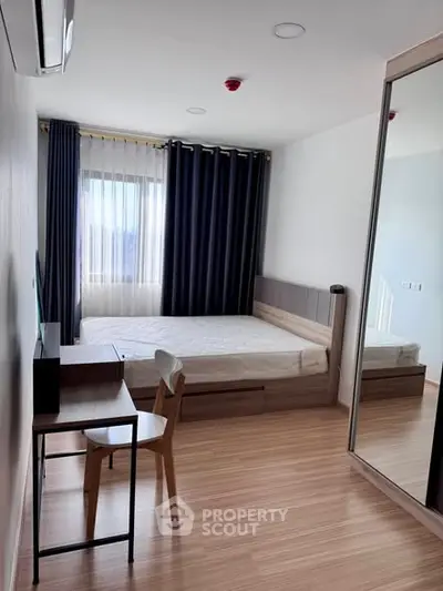 Modern bedroom with wooden flooring, large window, and stylish furniture in a cozy apartment.