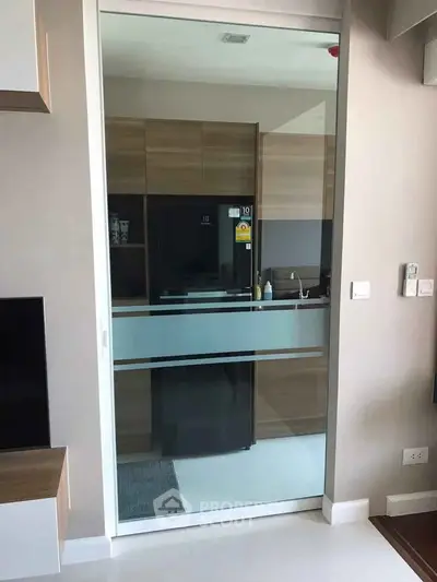 Modern kitchen with sleek glass door and wooden cabinetry, featuring a stylish refrigerator and minimalist design.