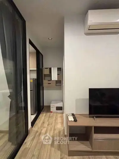 Modern living room with wooden flooring, TV, and air conditioning in a stylish apartment.
