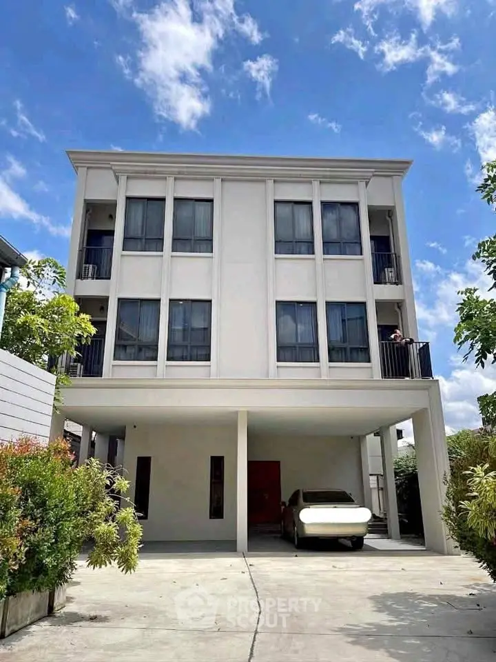 Modern three-story building with carport and lush greenery under a clear blue sky.
