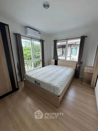 Modern bedroom with large windows and wooden flooring, featuring a comfortable bed and air conditioning.