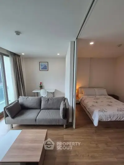 Modern studio apartment with cozy living area and bedroom, featuring wooden flooring and natural light.