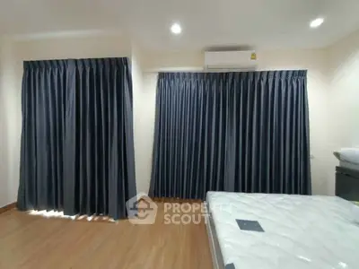Spacious bedroom with wooden flooring and dark curtains, featuring air conditioning.