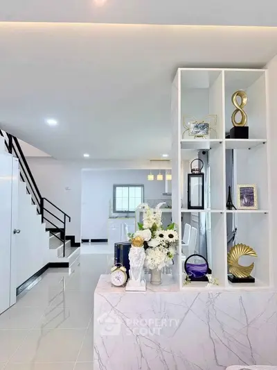 Modern living room with elegant decor and open layout, featuring stylish shelving and sleek staircase.