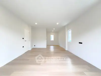 Spacious empty room with wooden flooring and white walls, ideal for customization.