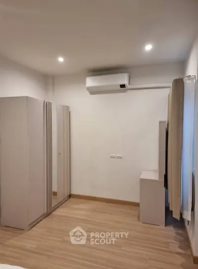 Modern bedroom with sleek wardrobe and air conditioning, featuring minimalist design and wooden flooring.
