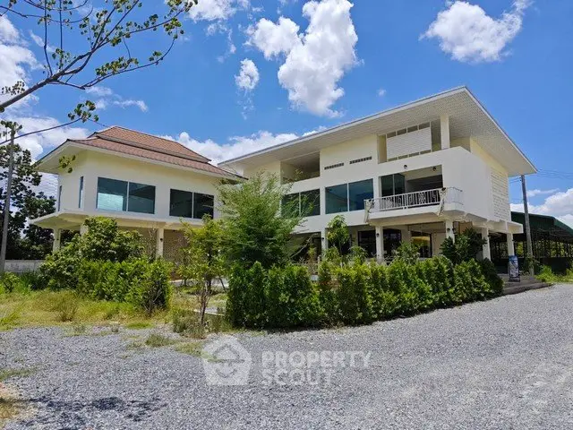 Modern two-story house with large windows and lush greenery under a bright blue sky.