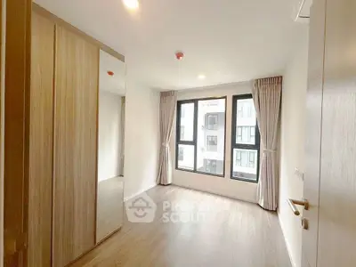 Spacious bedroom with large windows and modern wooden wardrobe in a bright apartment.