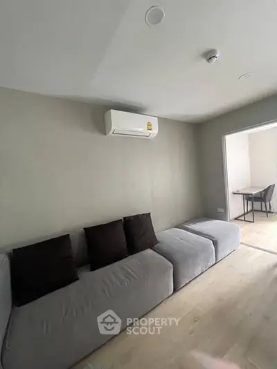 Modern living room with grey sofa and air conditioning unit, minimalistic design.