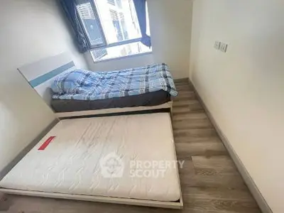 Cozy bedroom with single bed and extra mattress, bright window view.