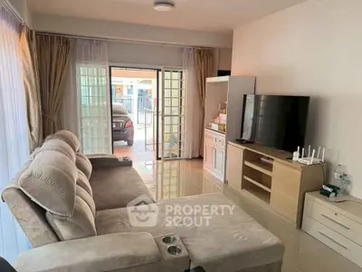 Spacious living room with modern sofa and large TV, featuring sliding glass doors leading to a patio.