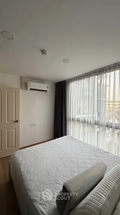 Modern bedroom with large window and air conditioning, featuring elegant curtains and a comfortable bed.