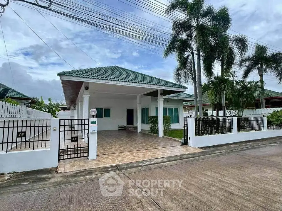 Charming single-story house with green roof and spacious driveway in tropical setting.