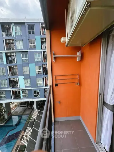 Modern apartment balcony with vibrant orange wall and pool view, featuring air conditioning unit and railing.