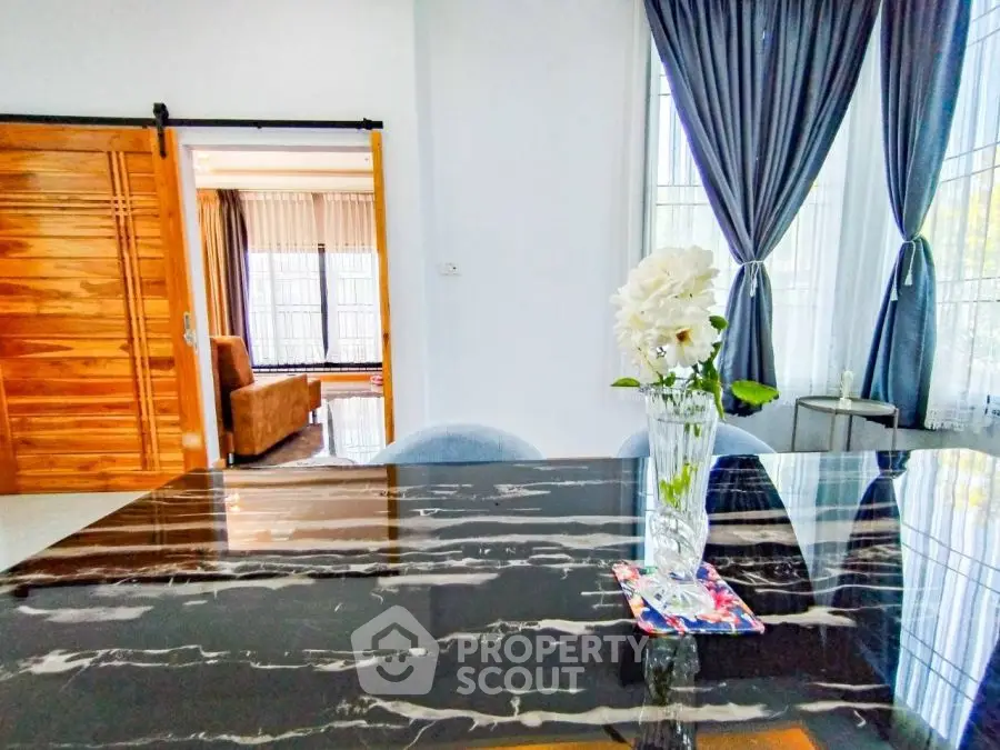 Elegant dining area with marble table and floral centerpiece, adjacent to cozy living room.