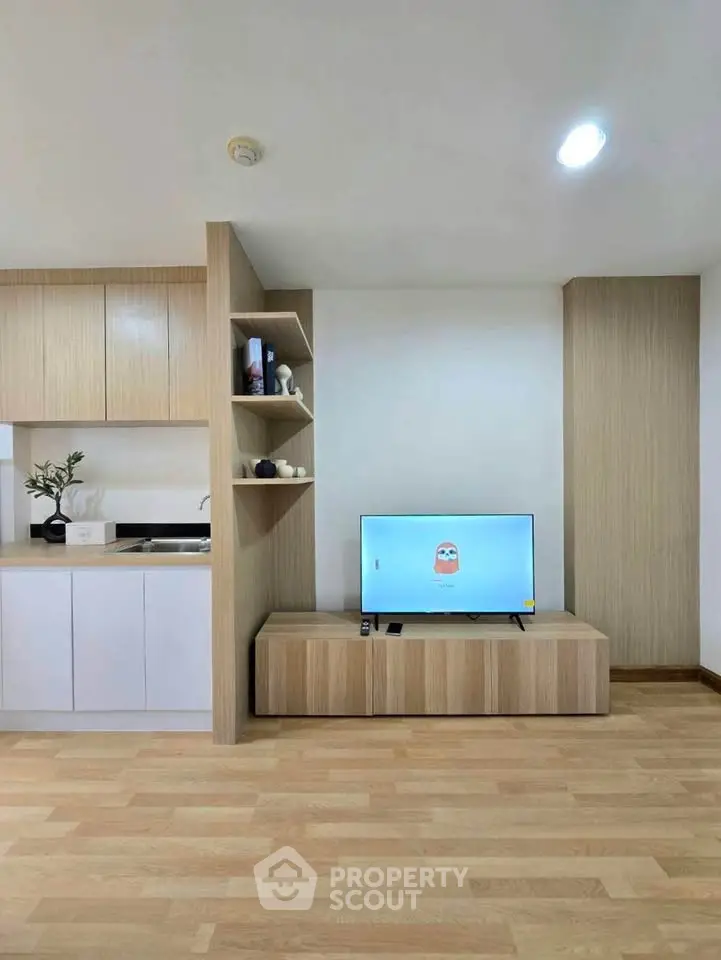 Modern living room with sleek wooden cabinetry and flat-screen TV, open kitchen layout.