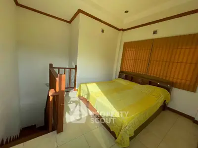 Cozy bedroom with natural light and wooden accents, featuring a staircase and a comfortable bed.
