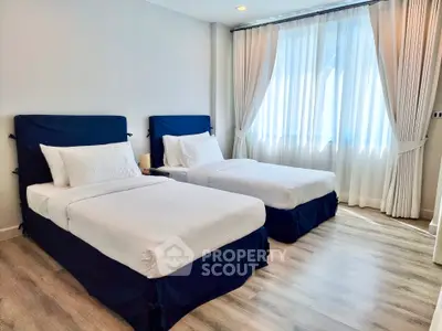 Bright and inviting bedroom with two single beds, elegant drapery, and modern flooring, perfect for a comfortable living experience.