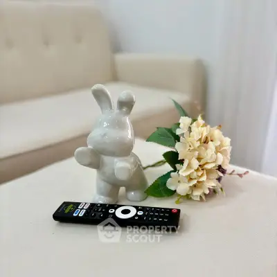 Charming living room detail with cozy sofa, decorative bunny, and remote control on a soft ottoman.