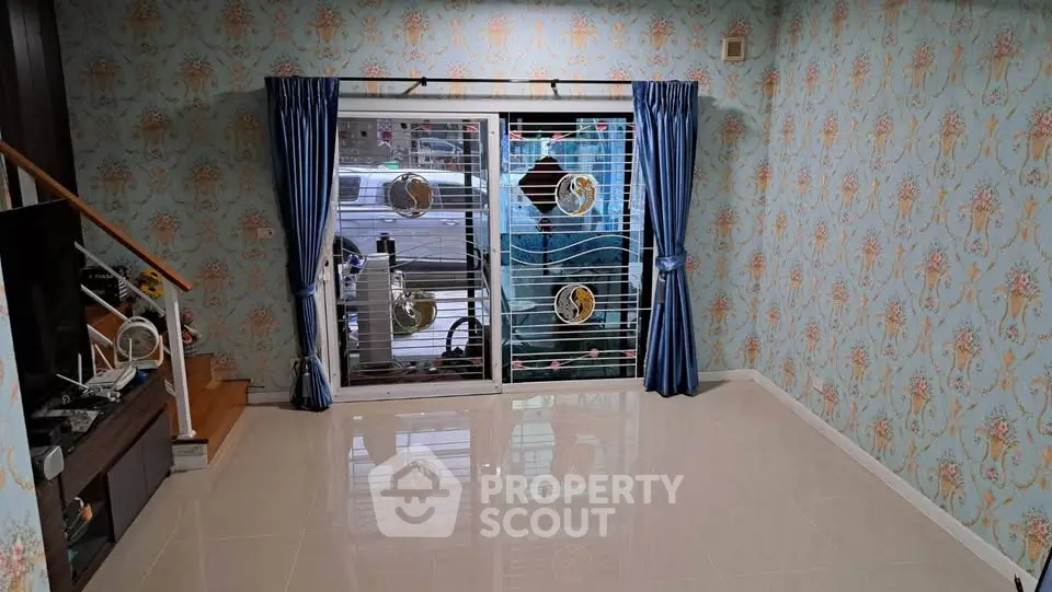 Charming living room with elegant wallpaper and glossy tile flooring, featuring a secure sliding door with decorative grill.