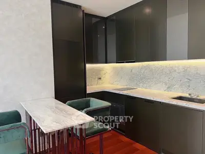 Modern kitchen with sleek dark cabinets and marble countertops, featuring a stylish breakfast bar and elegant seating.