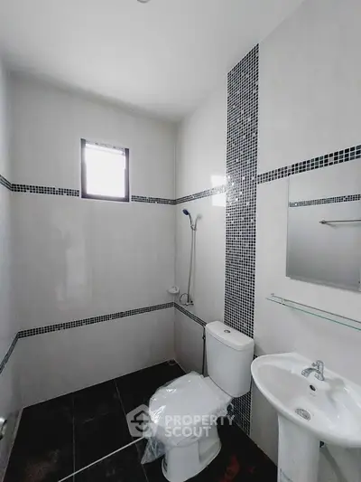 Modern bathroom with sleek design and tiled accents, featuring a toilet, sink, and shower area.
