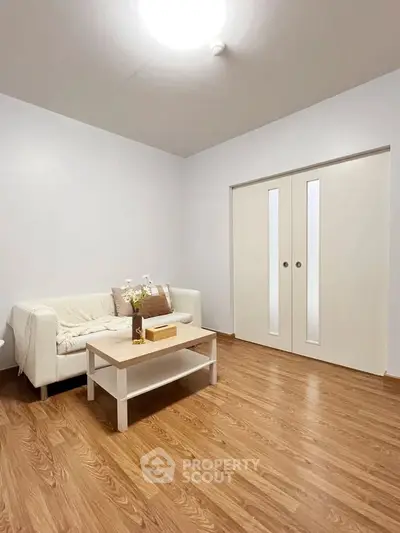 Minimalist living room with wooden flooring and cozy white sofa.