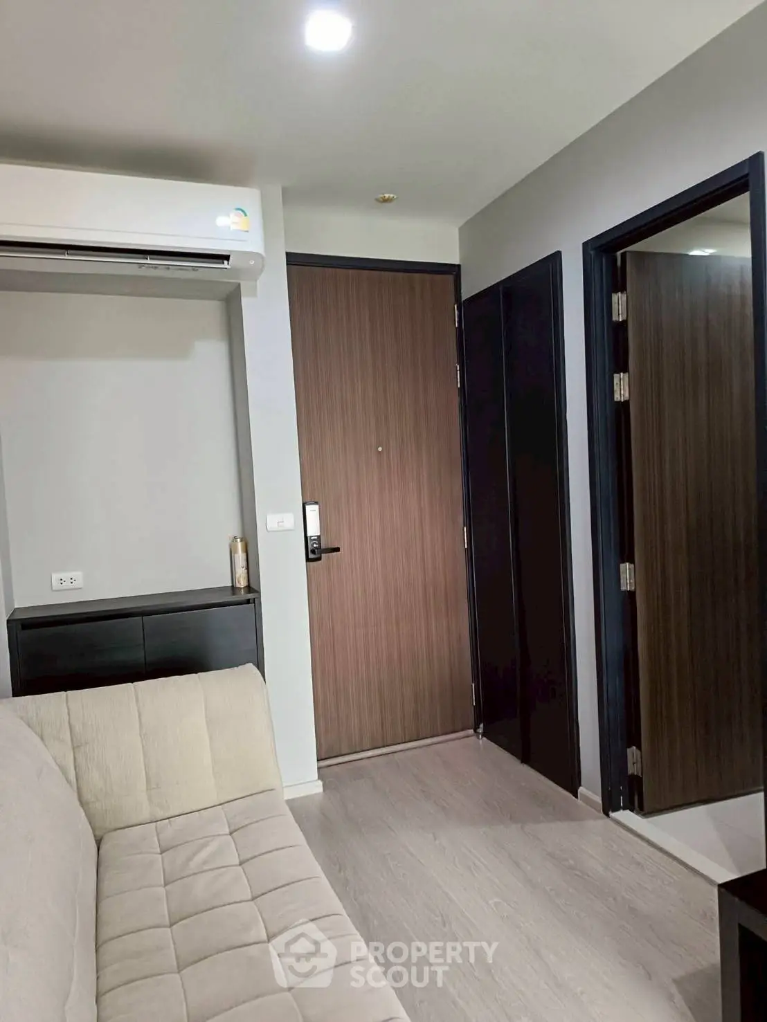 Modern living room with sleek design and air conditioning, featuring a comfortable sofa and wooden door.