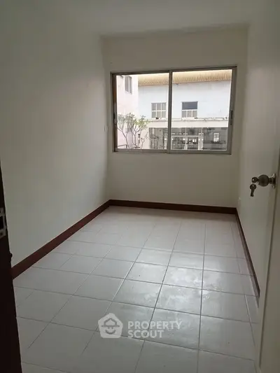 Spacious empty room with large window and tiled floor, perfect for customization.