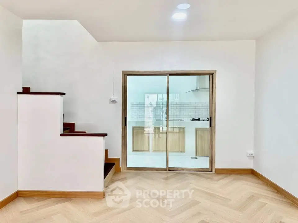 Modern interior with wooden staircase and sliding glass doors leading to a bright kitchen.