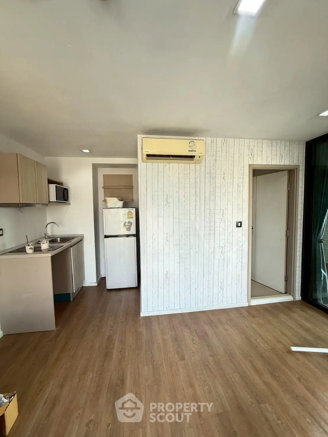 Modern apartment interior with wooden flooring and compact kitchen area featuring fridge and microwave.