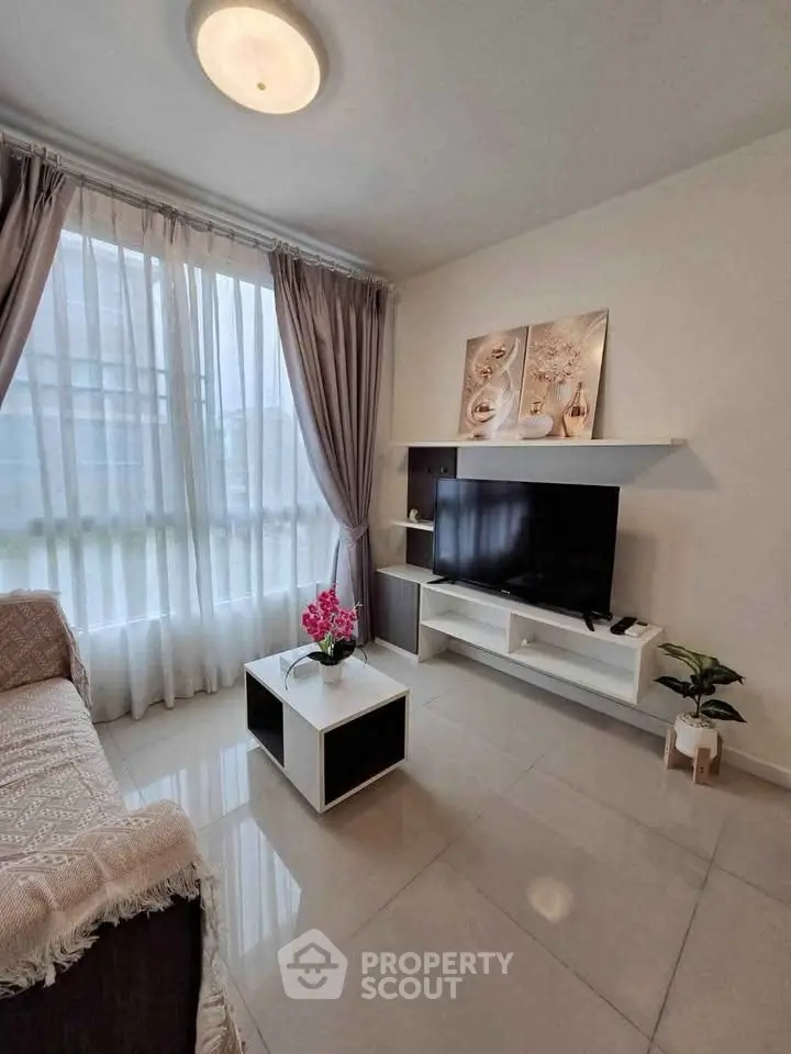 Modern living room with sleek TV setup and elegant decor, featuring large windows and stylish furniture.